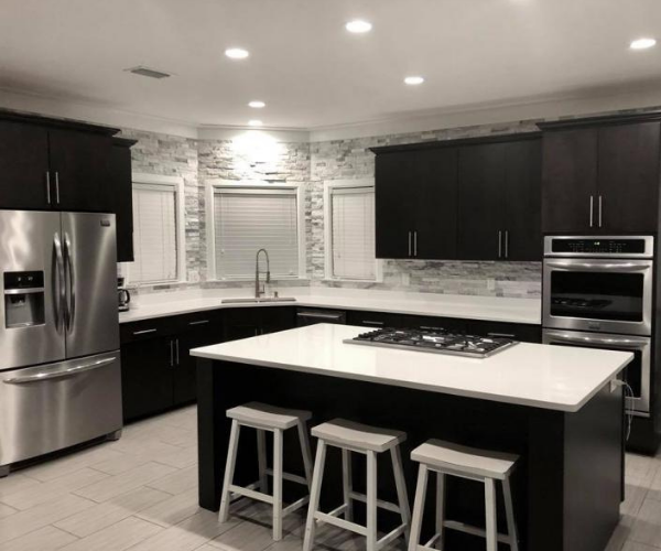 Modern kitchen with dark cabinets, white countertops, a center island with bar stools, and stone-tiled walls.