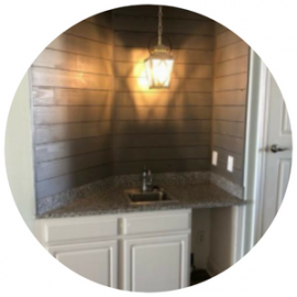 A wet bar nook with white cabinets, speckled granite countertops, a small sink, shiplap walls, and a hanging lantern light.