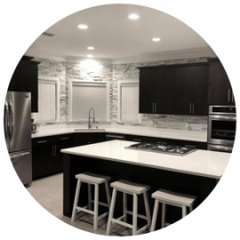 Modern kitchen with dark cabinets, white countertops, a center island with bar stools, and a stone tile backsplash.