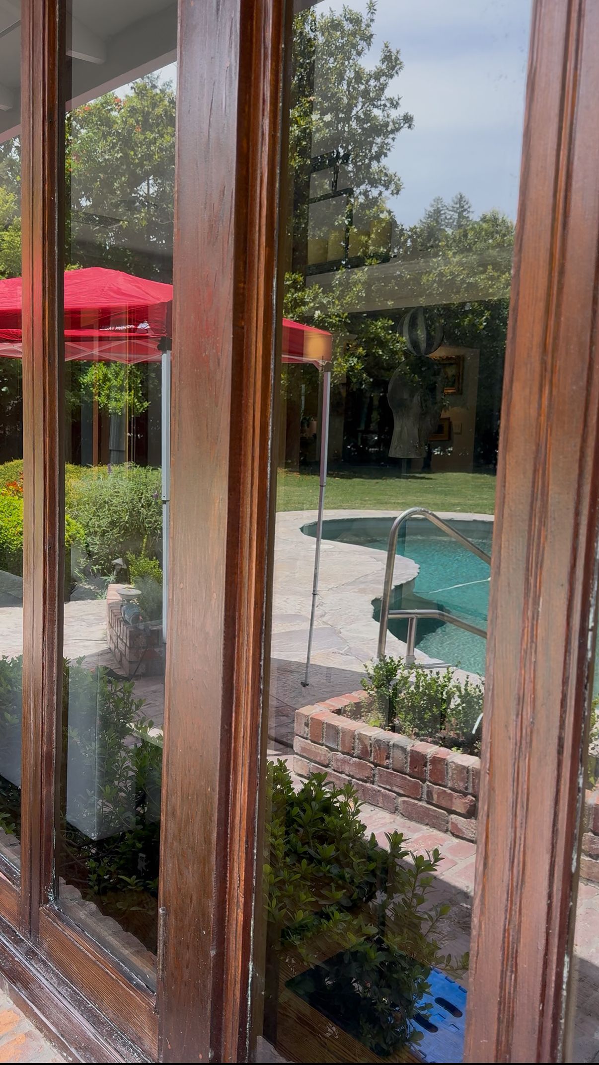 View through a window: red umbrella, pool, and green foliage.