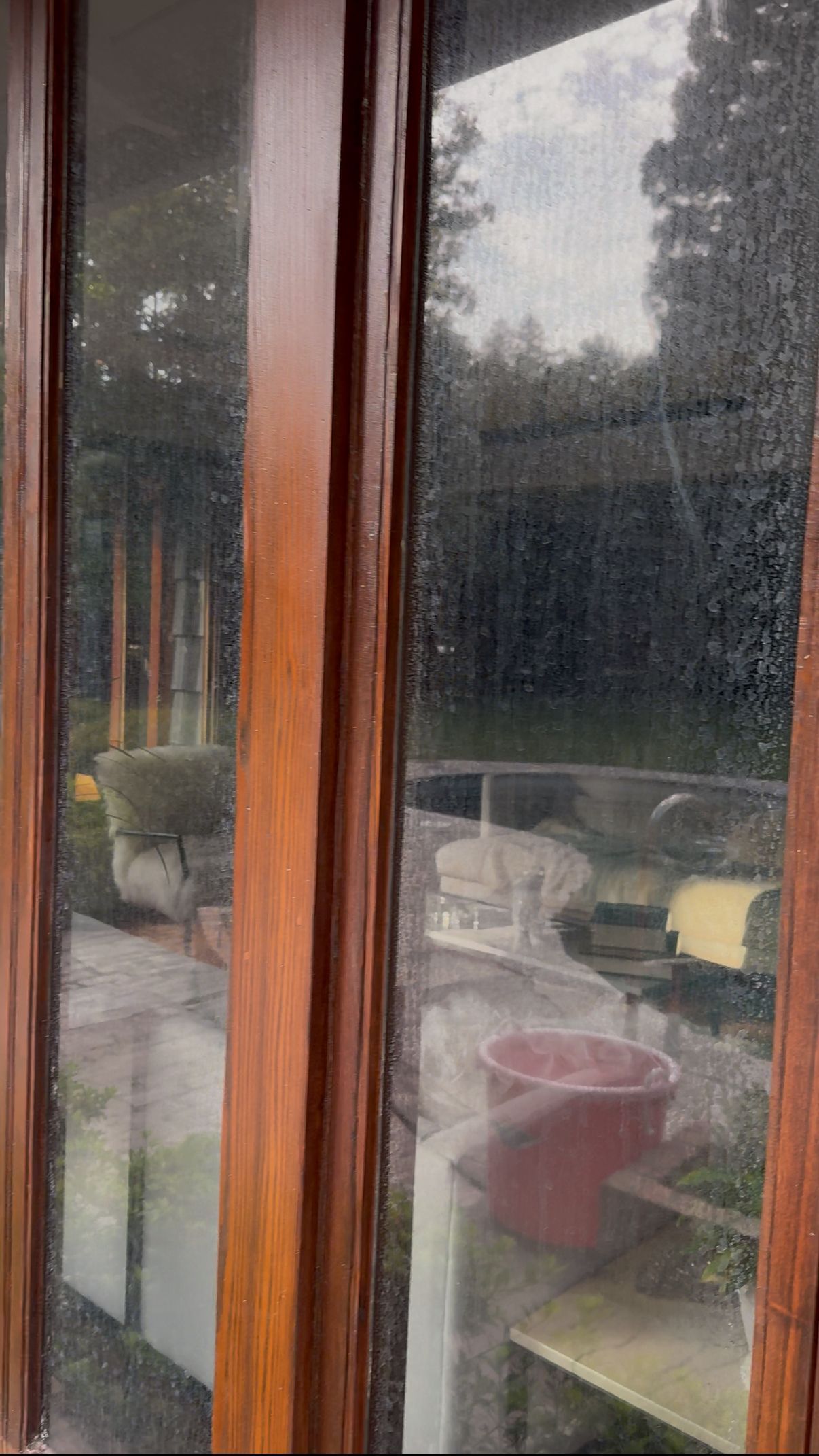 Wooden window frame with a blurry view of a patio and garden. Raindrops are visible on the glass.