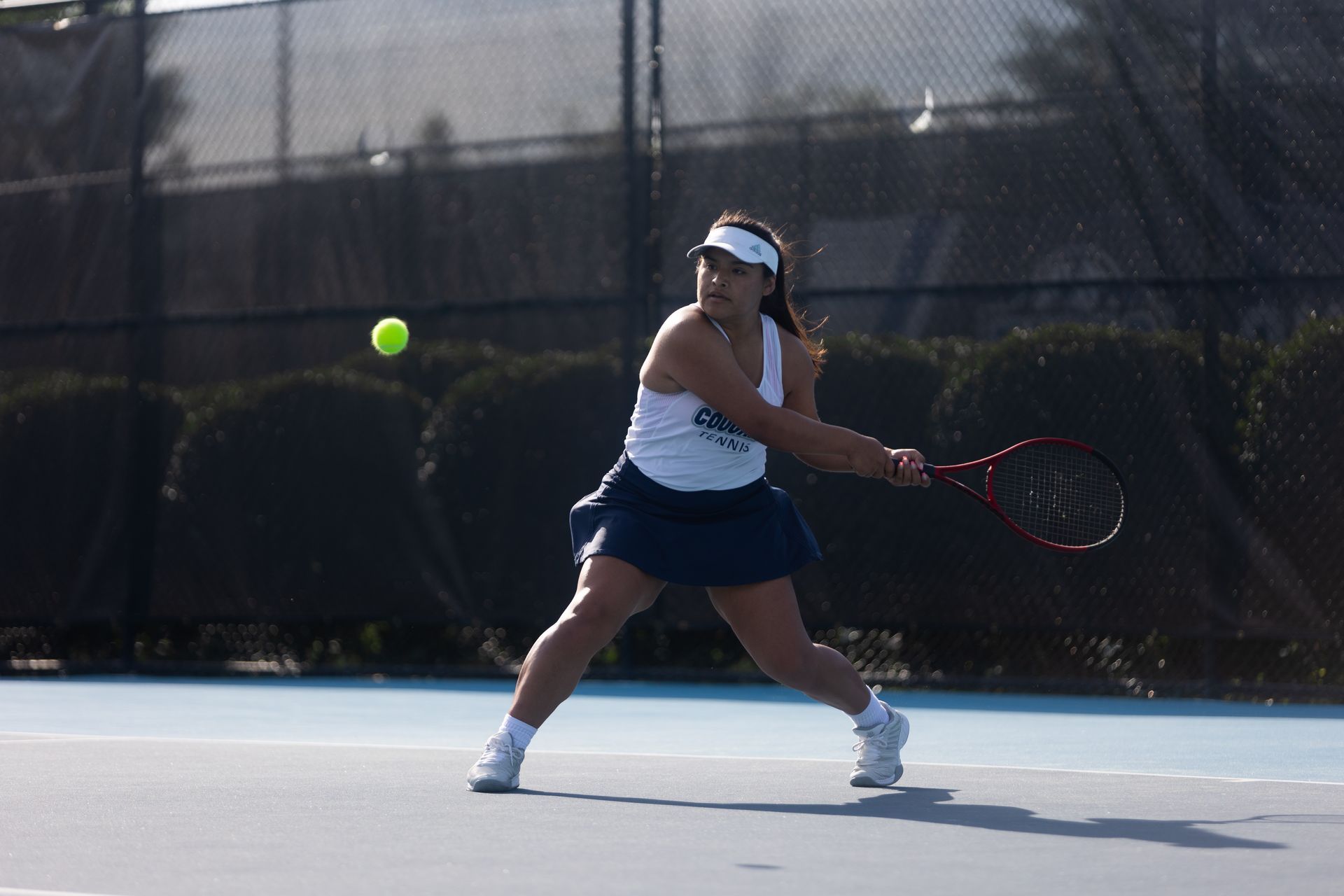 Tennis player in white and navy outfit hitting a backhand on an outdoor court