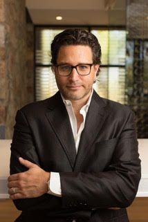 A man in a suit and glasses is standing with his arms crossed.