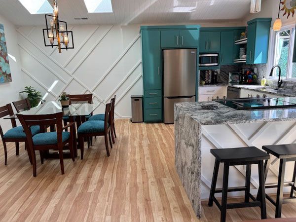 Spacious kitchen and dining area with teal cabinets, a granite countertop, and wooden floors. A dining table and chairs are on the left side.