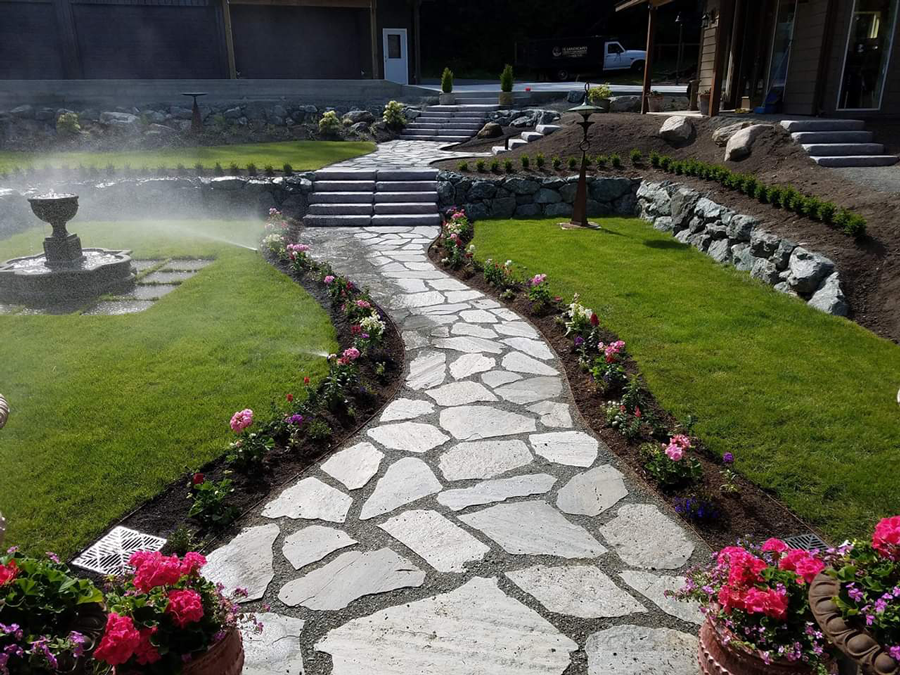 a stone walkway in a garden with flowers and a fountain .