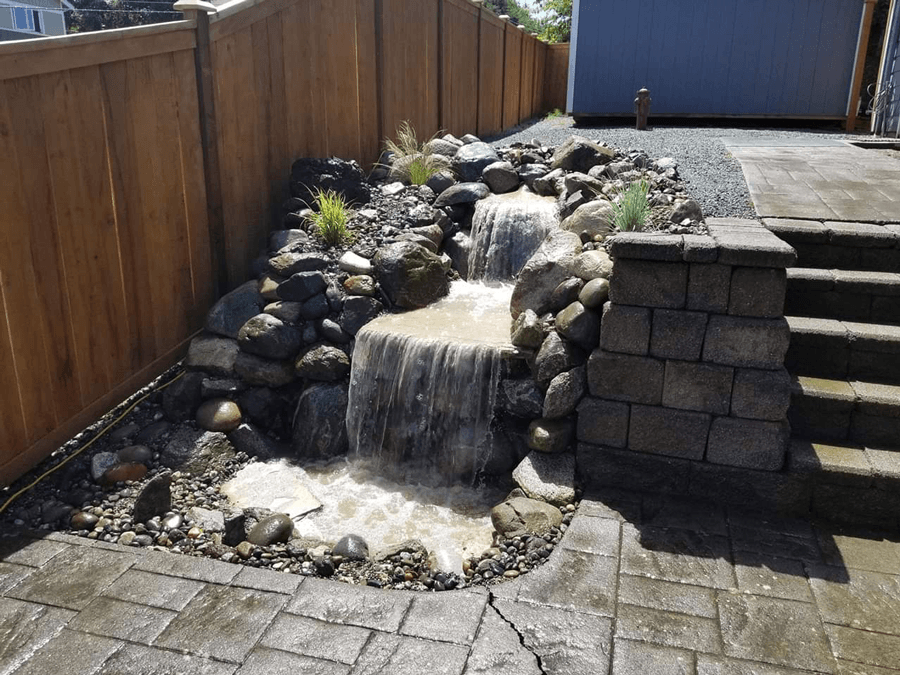 a small waterfall is surrounded by rocks and a wooden fence .