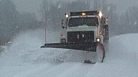 Snow Removal Services. A plow truck moving snow on a commercial parking lot.