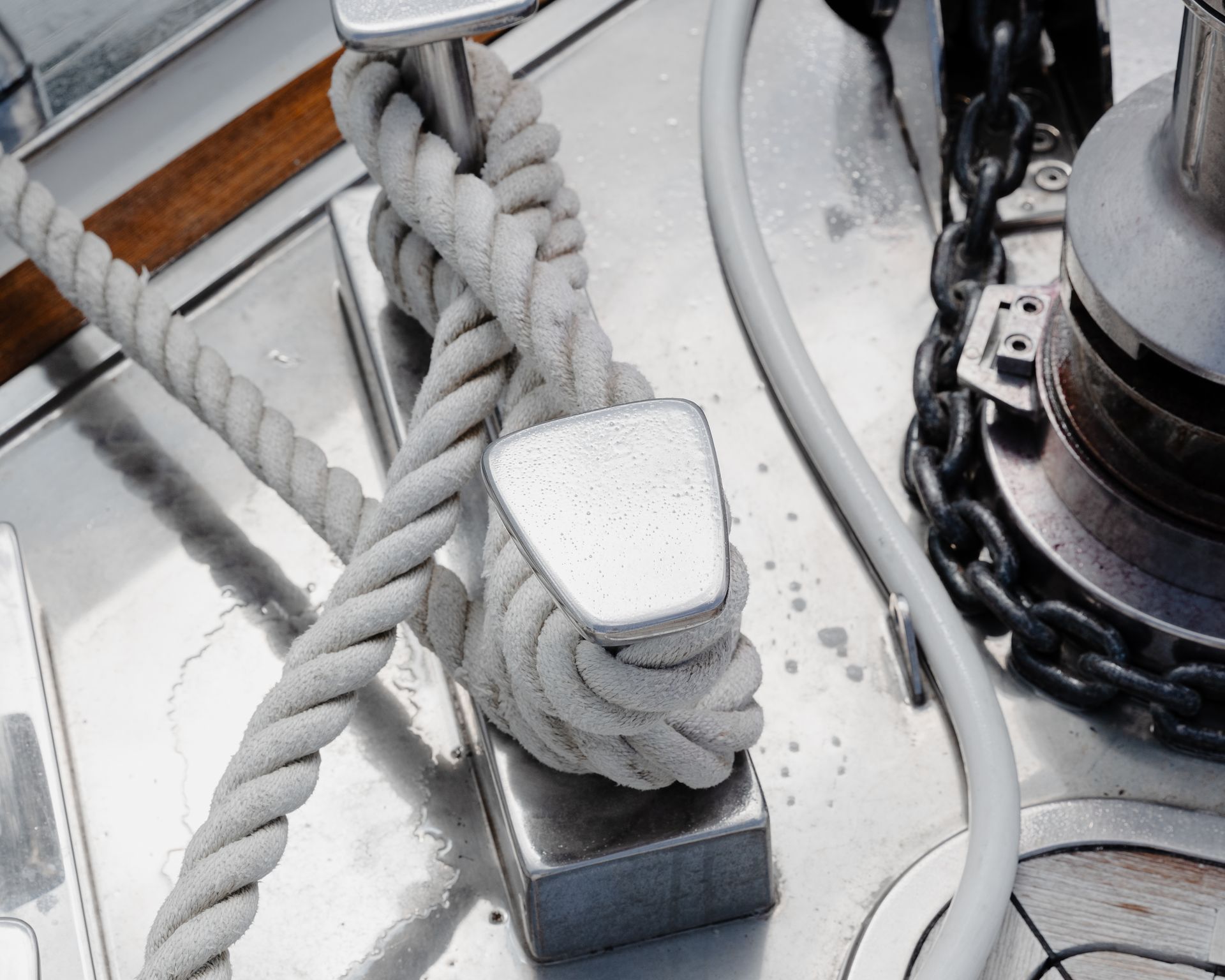 Coiled white rope tied around a metal cleat on a boat deck beside chain and rigging lines