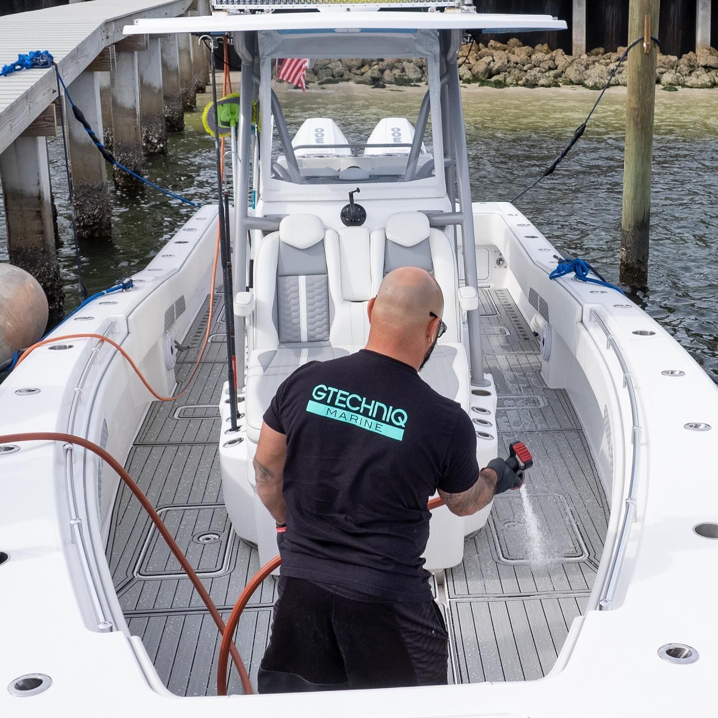 Person cleaning a white boat deck with a red hose at a dock.