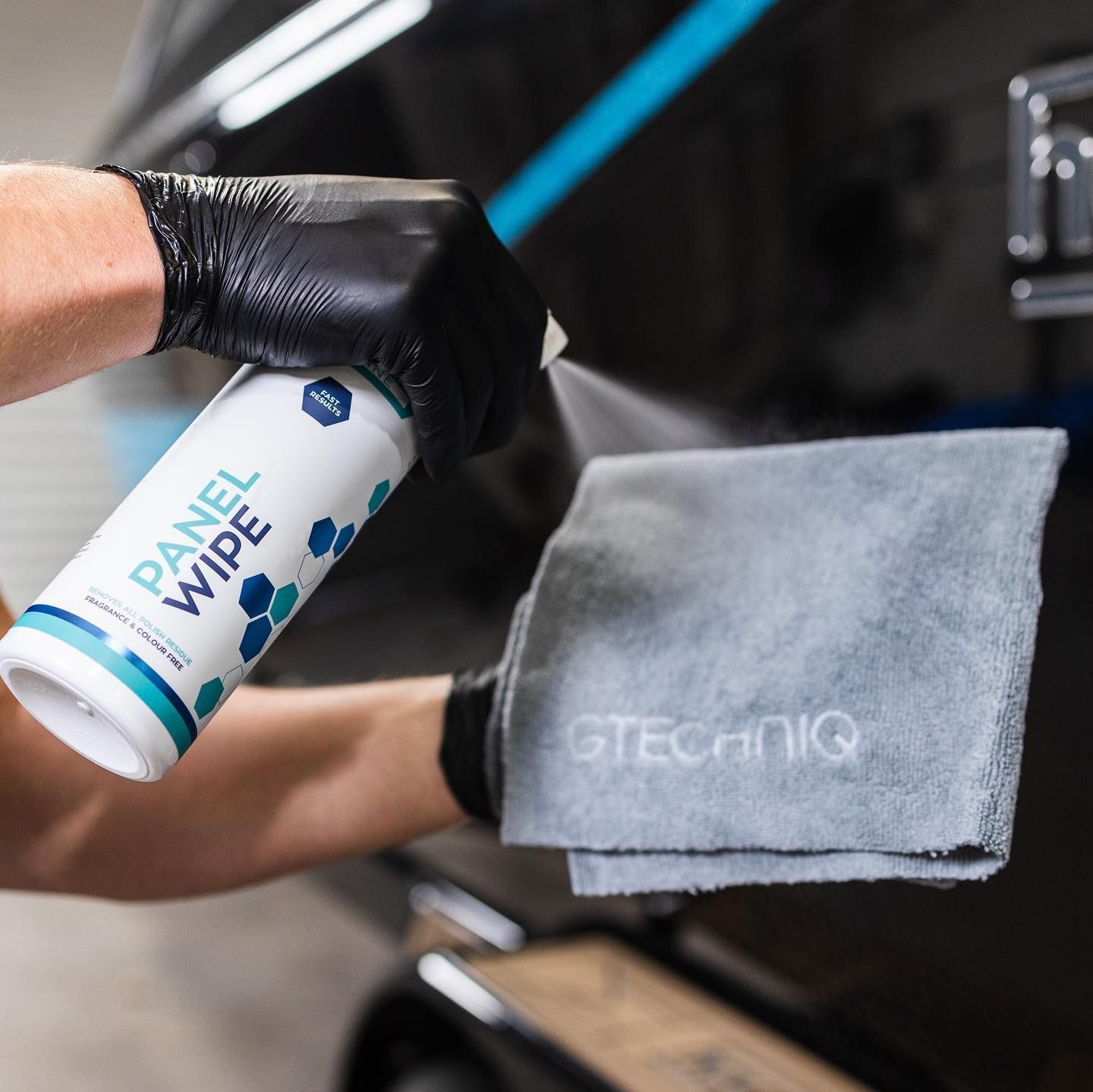 Gloved hand using Armor All wipe on a gray microfiber cloth beside a car interior.