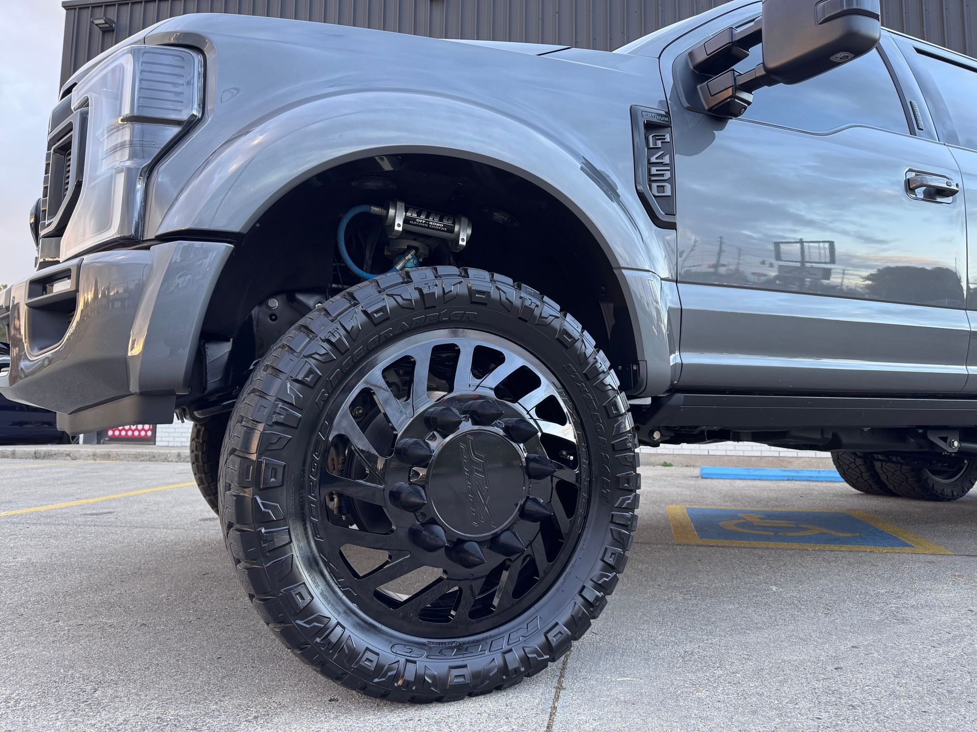 A gray truck with black wheels and tires is parked in a parking lot.