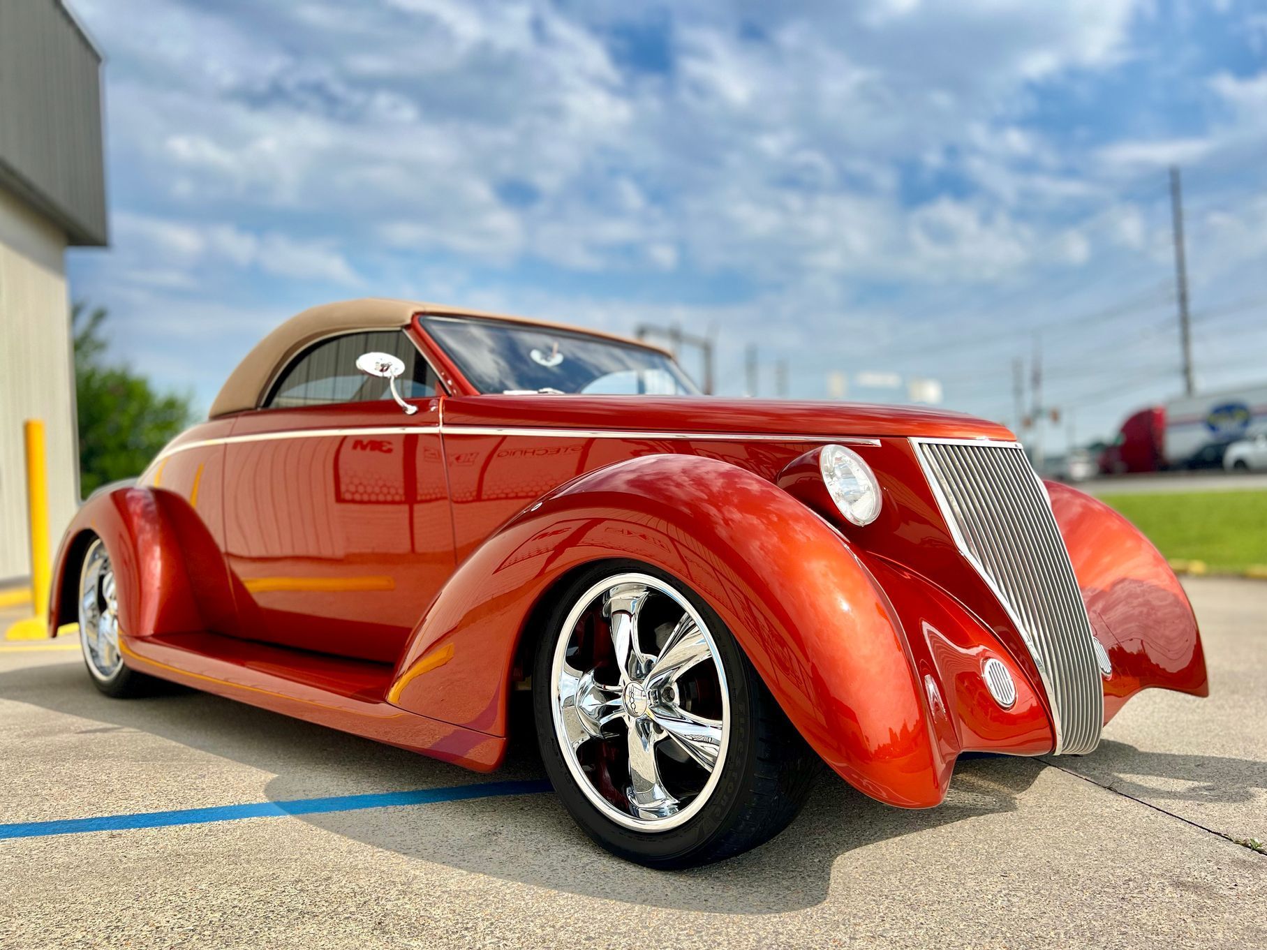 Orange custom hot rod with tan convertible top, parked outside.