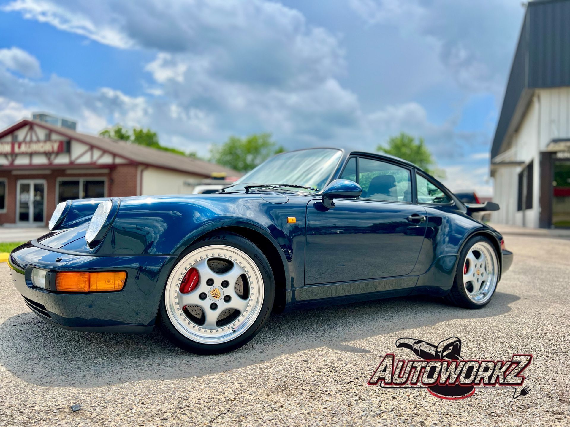 A blue porsche 911 is parked in front of a building.