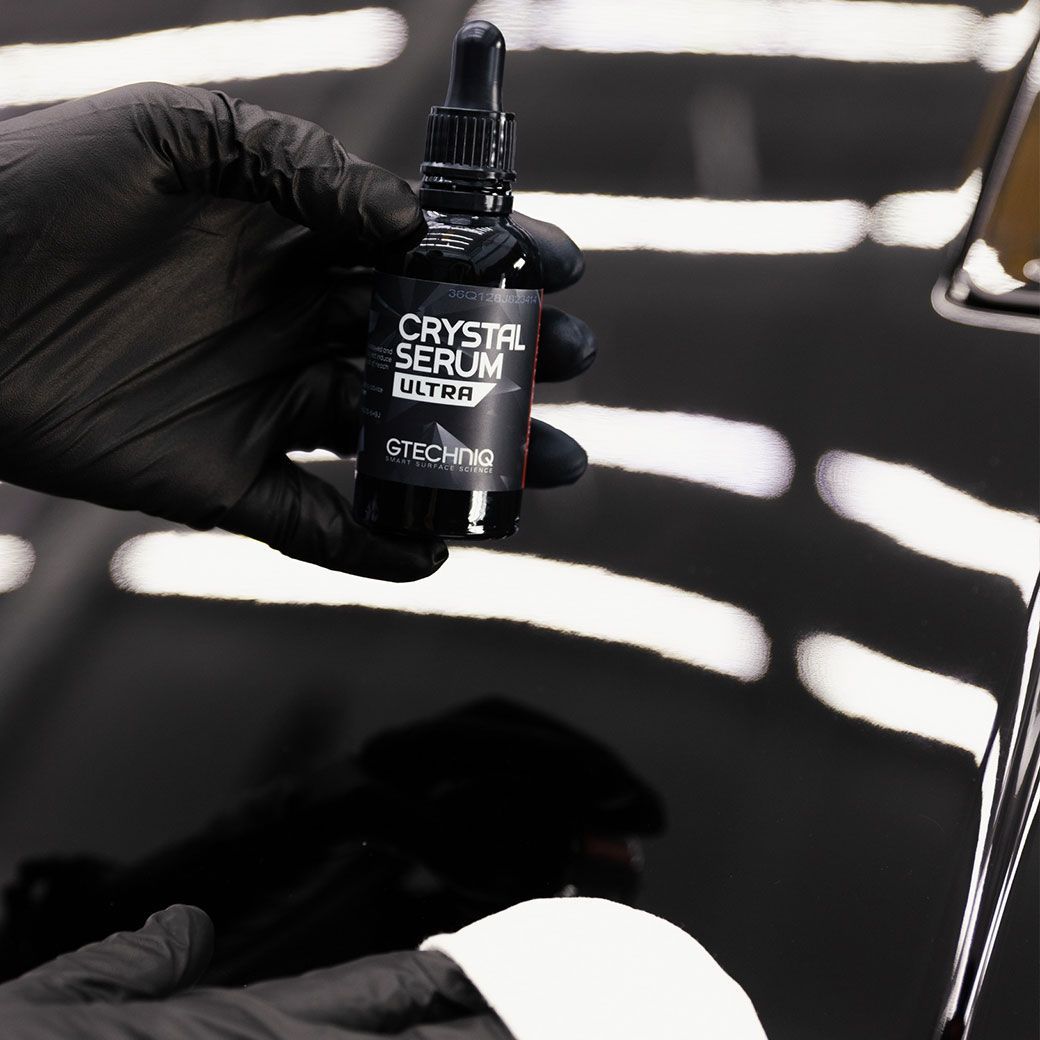 A person wearing black gloves is holding a bottle of crystal serum