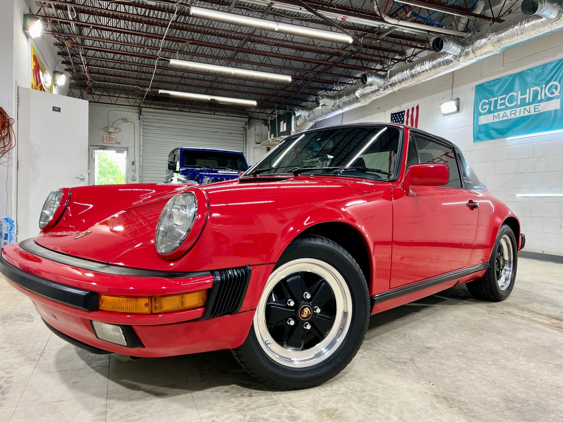 Red Porsche 911 Targa sports car in a garage setting with a black roof and black and white wheels.