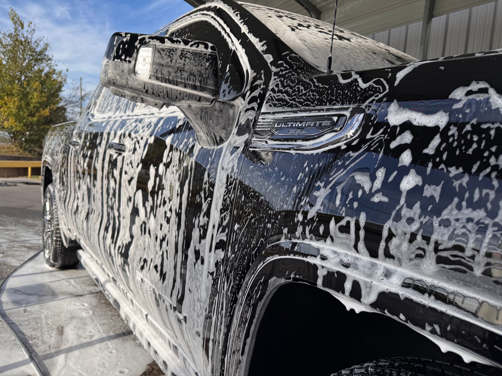 A black car is covered in soap foam at a car wash.