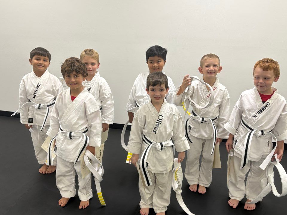 Group of young children in karate uniforms, holding belts, smiling.
