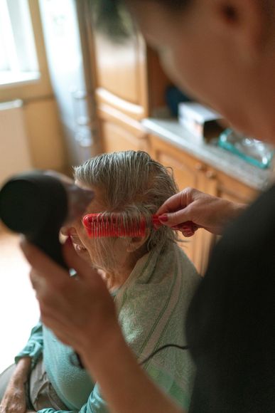 Person using a hair dryer and brush on another's wet hair indoors.