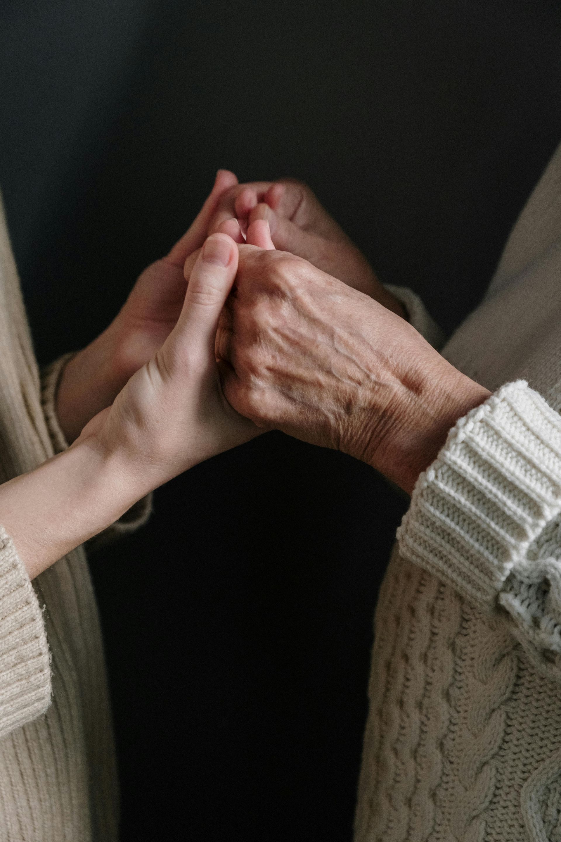 Two people holding hands; one with wrinkled skin, wearing a cream sweater.