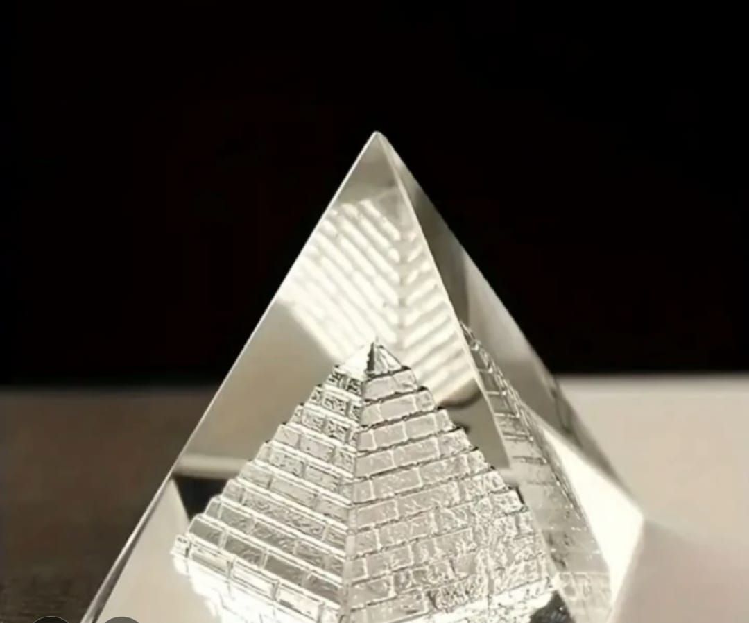 Una pirámide de vidrio con una pirámide más pequeña grabada en su interior, sobre una superficie reflectante.