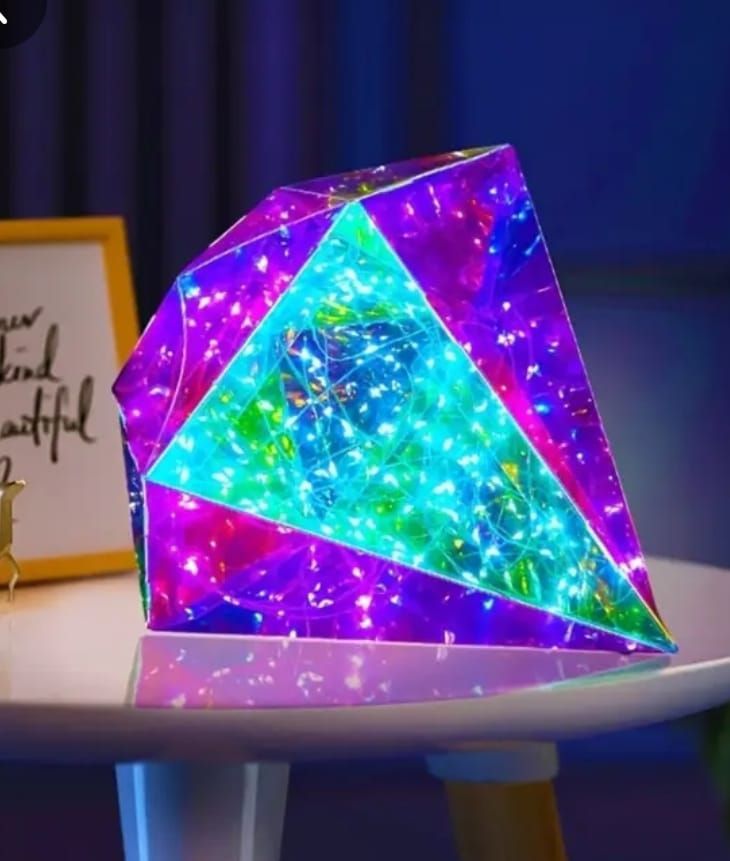 Lámpara de prisma geométrico con luces de colores sobre una mesa blanca.