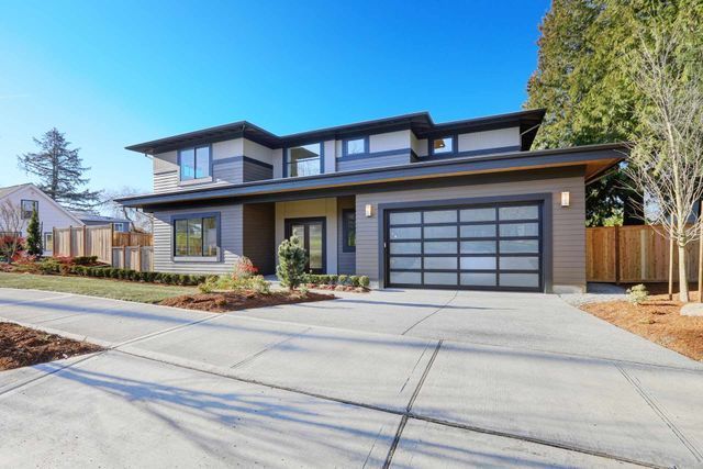 Modern two-story suburban home with a multi-paneled glass garage door and a concrete driveway under a clear blue sky.