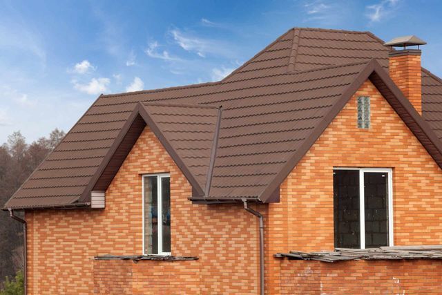 A brown-roofed brick house with two dormer windows under a bright blue sky.