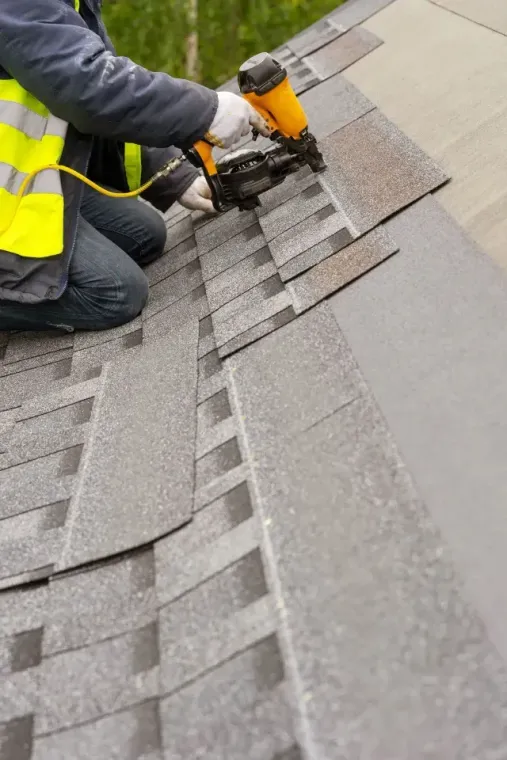 Roofing company installing shingles with a nail gun on a sloped roof in Aurora, IL.