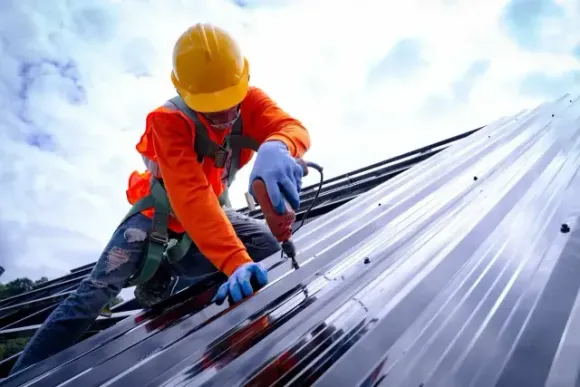 Worker in hard hat and orange jacket from local roofing contractors in Aurora, IL securing a metal roof panel with a tool