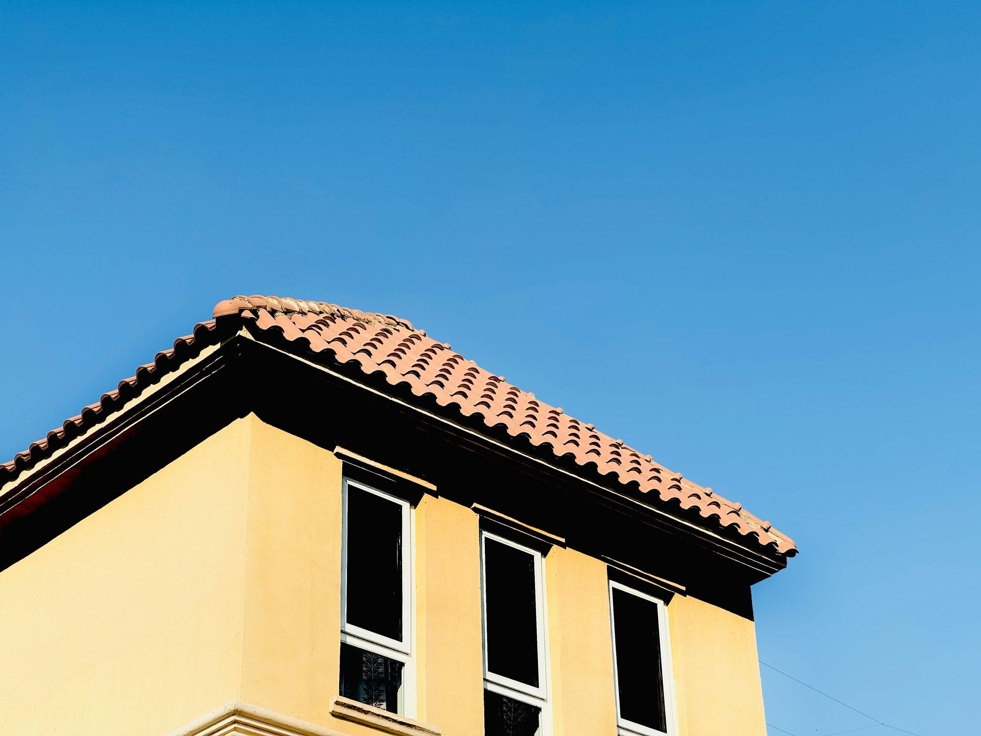 Two construction workers wearing safety vests and hard hats install solar panels on a tiled residential roof.