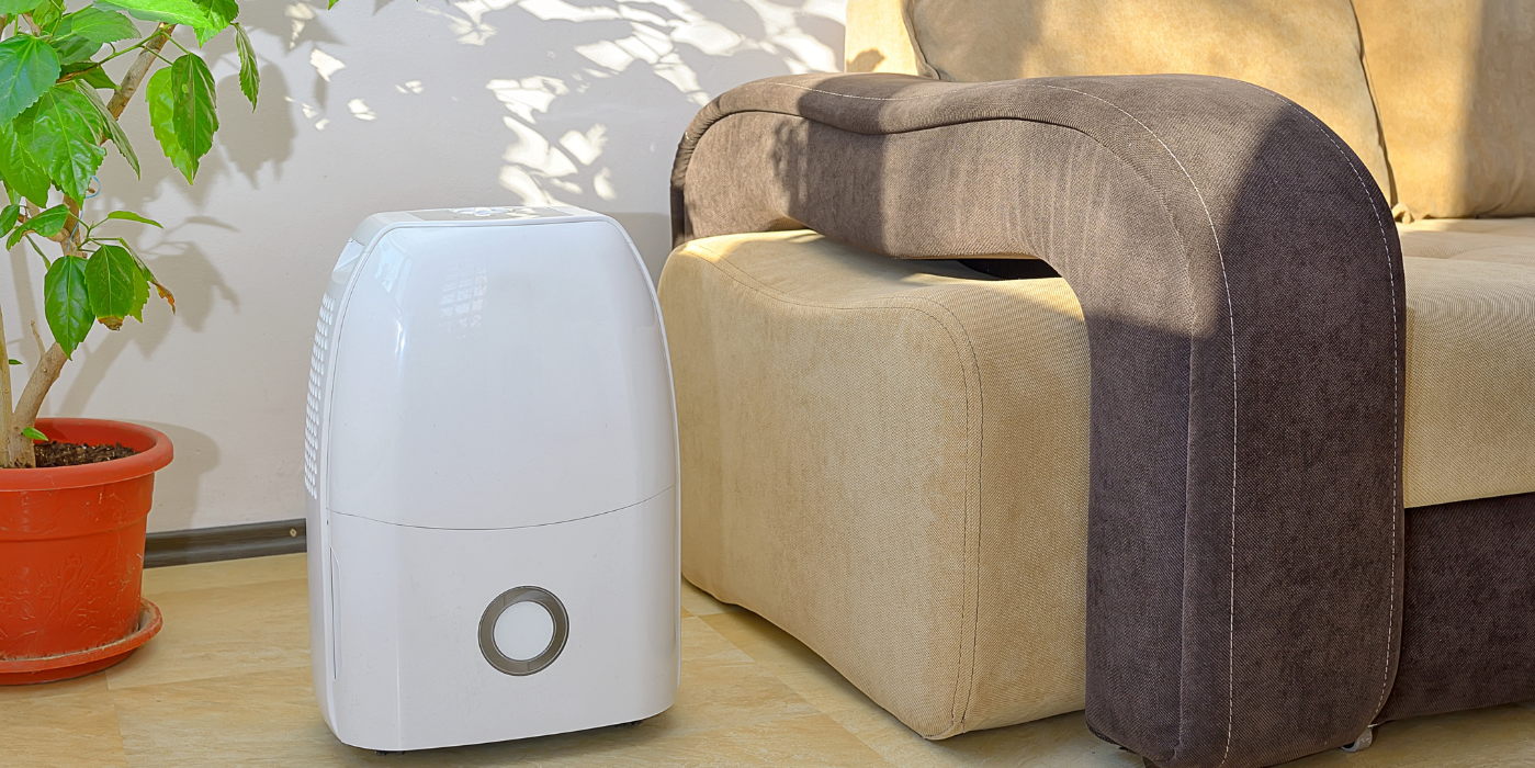 A white humidifier with a circular button, next to a beige sofa and a potted plant.