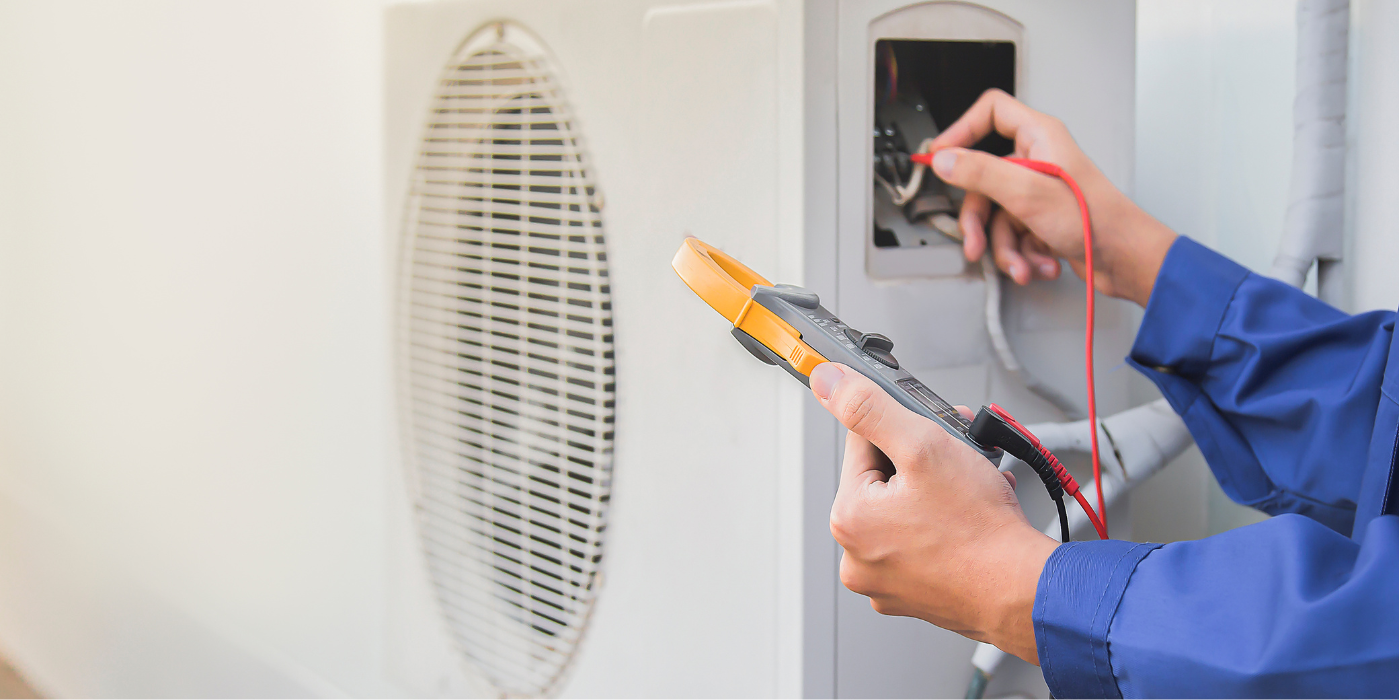 An electrician using a multimeter to check the electrical connections on an outdoor air conditioning unit.