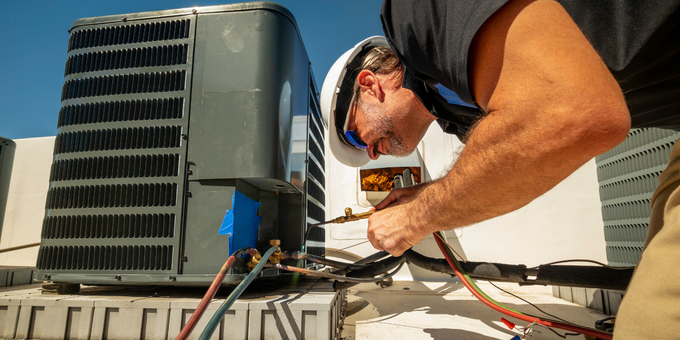 HVAC technician wearing a hard hat working on an AC unit on a rooftop.