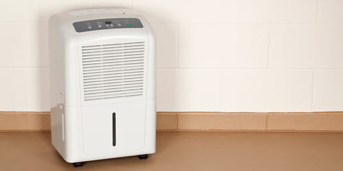 A white dehumidifier is sitting on the floor next to a wall.