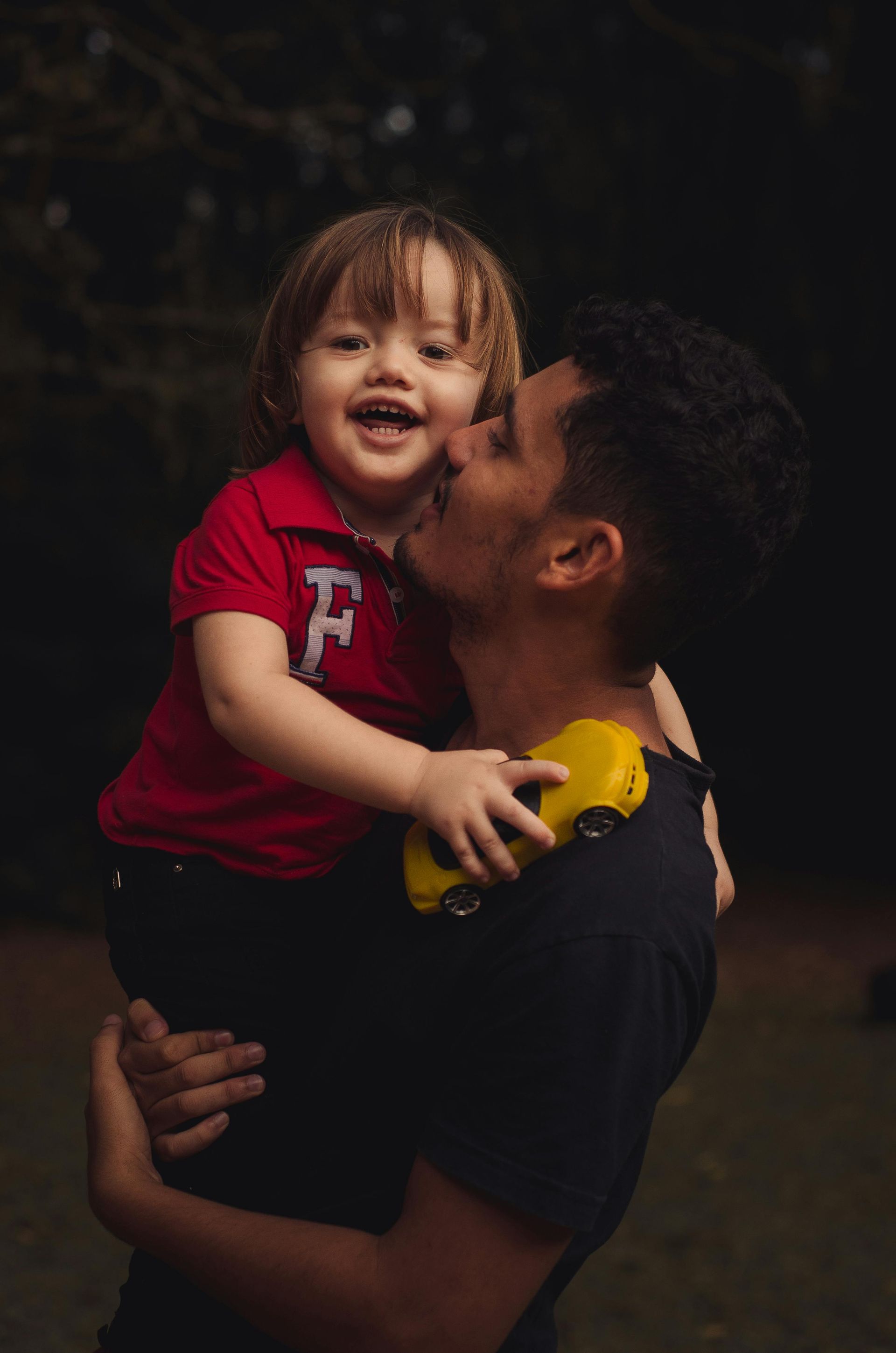 A man is kissing a little boy on the cheek while holding a toy car.