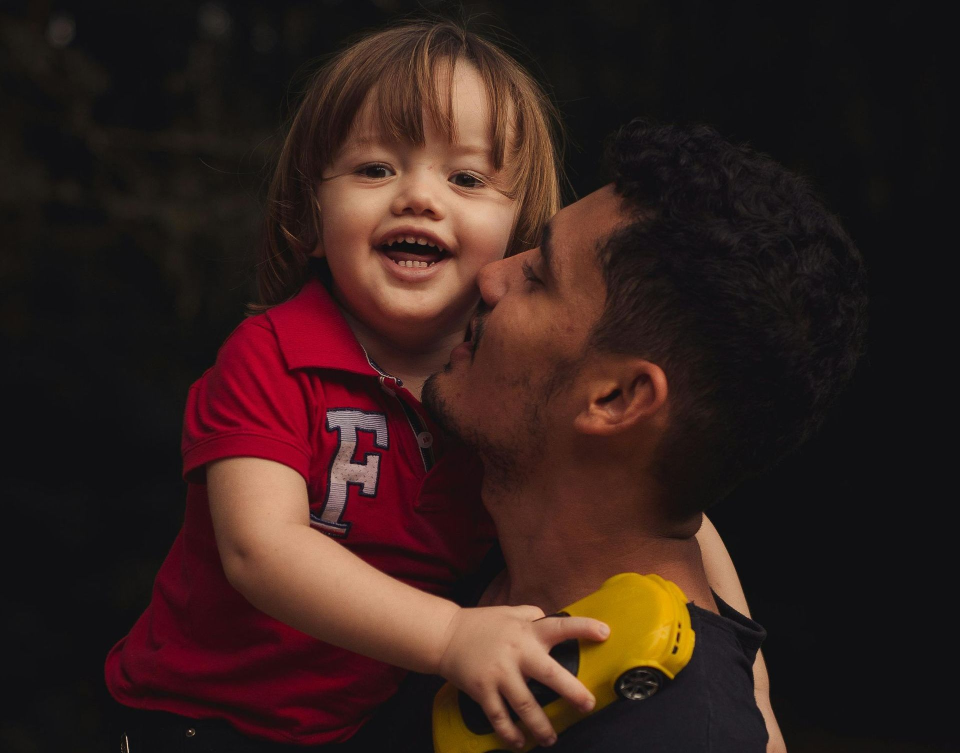 A little boy is kissing a man on the cheek while holding a toy car.