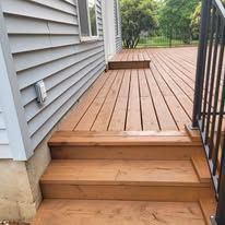 A set of wooden stairs leading up to a stained deck next to a house with light grey siding.