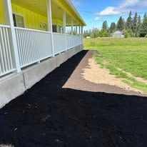 A yellow building with a white railing and concrete foundation, bordered by a dark mulched garden bed and green lawn.