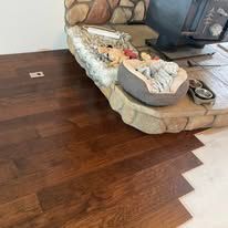 Dark hardwood flooring being installed, meeting a raised, stone-textured hearth with pet beds and bowls.