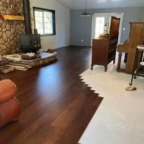 A transition between dark hardwood floors and light tile in a living room featuring a stone fireplace and a wooden piano.