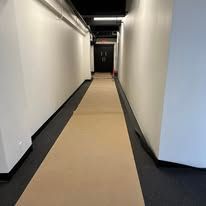 A narrow hallway with white walls, black trim, and a long protective paper runner leading to a black door.