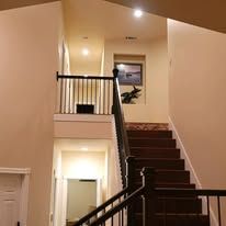 A staircase with dark wood steps and railings leads to an upper hallway with light walls and a framed art piece.