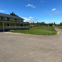 A two-story light yellow building with a covered porch sits beside an asphalt parking lot under a clear blue sky.