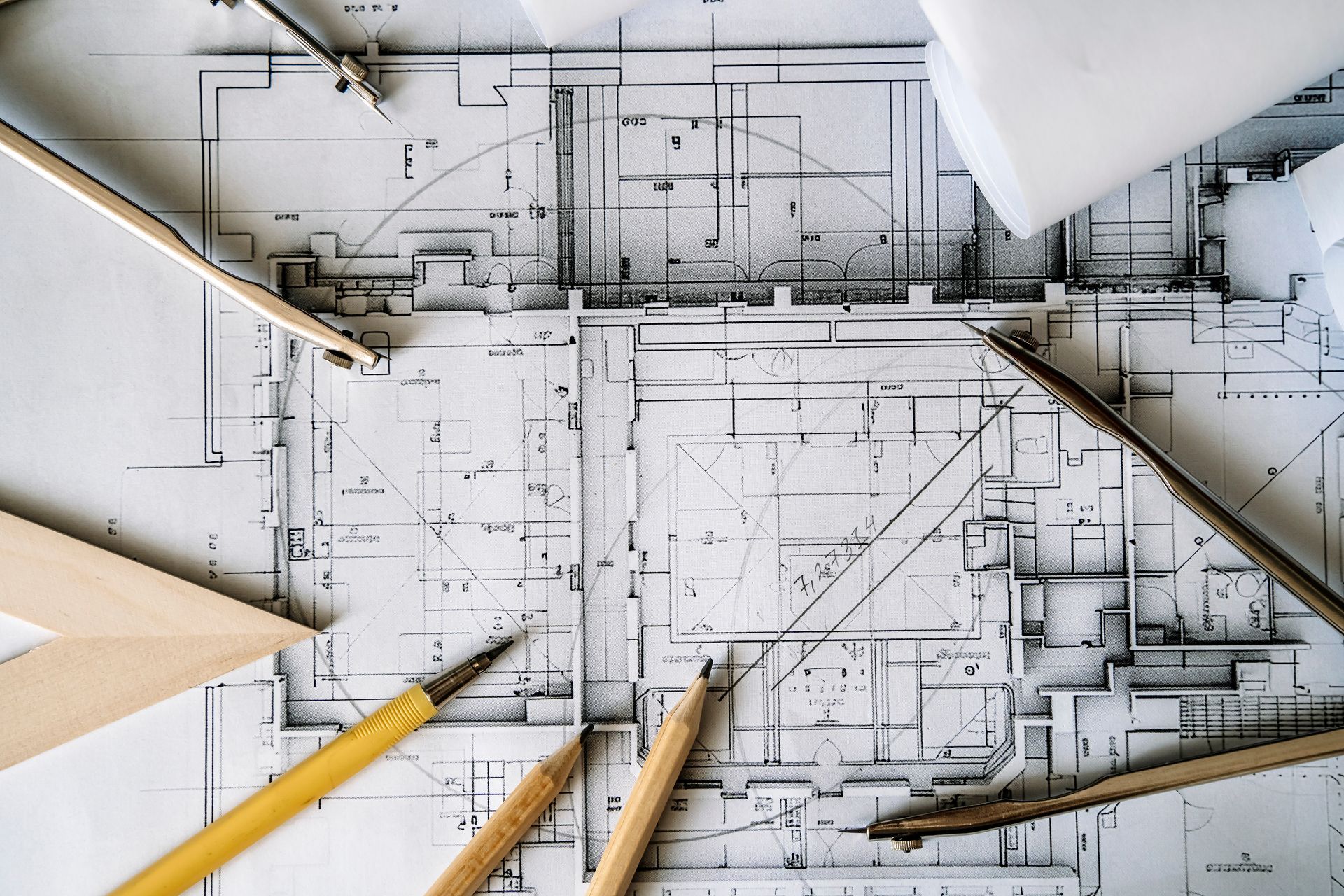 Architectural blueprints on a table with drafting pencils, a compass, and a ruler.
