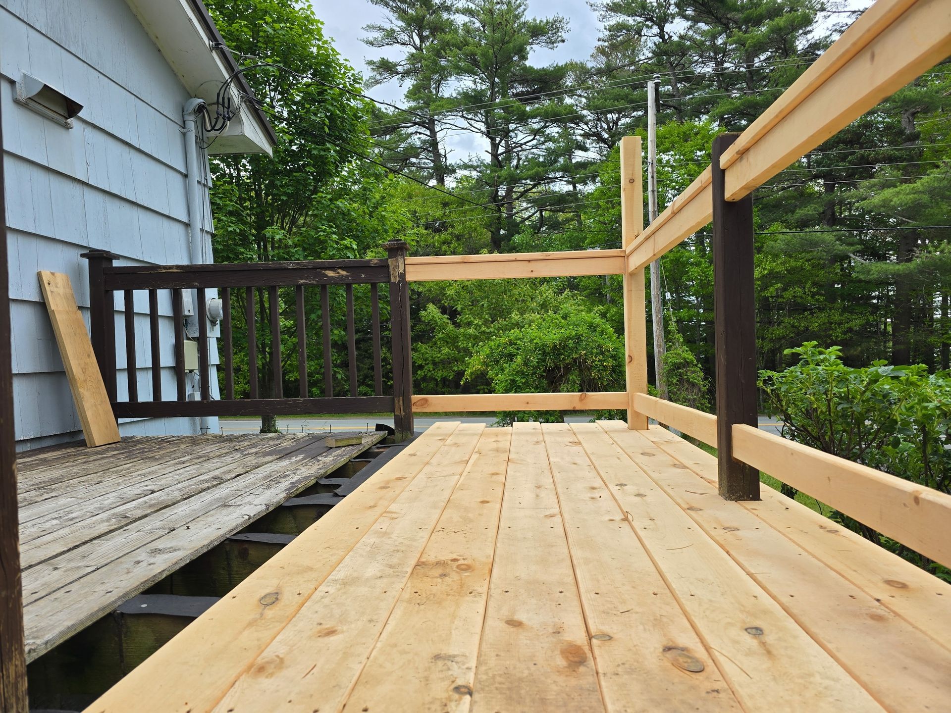 A partially renovated deck featuring new, light-colored wooden planks and railings alongside older, dark painted sections.