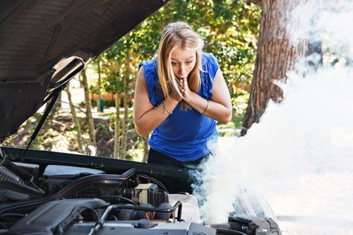 A woman is looking under the hood of a broken down car.