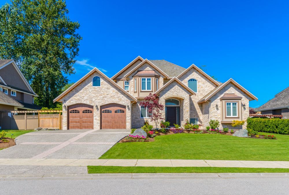 Two-story brick house with a three-car garage, green lawn, and blue sky.