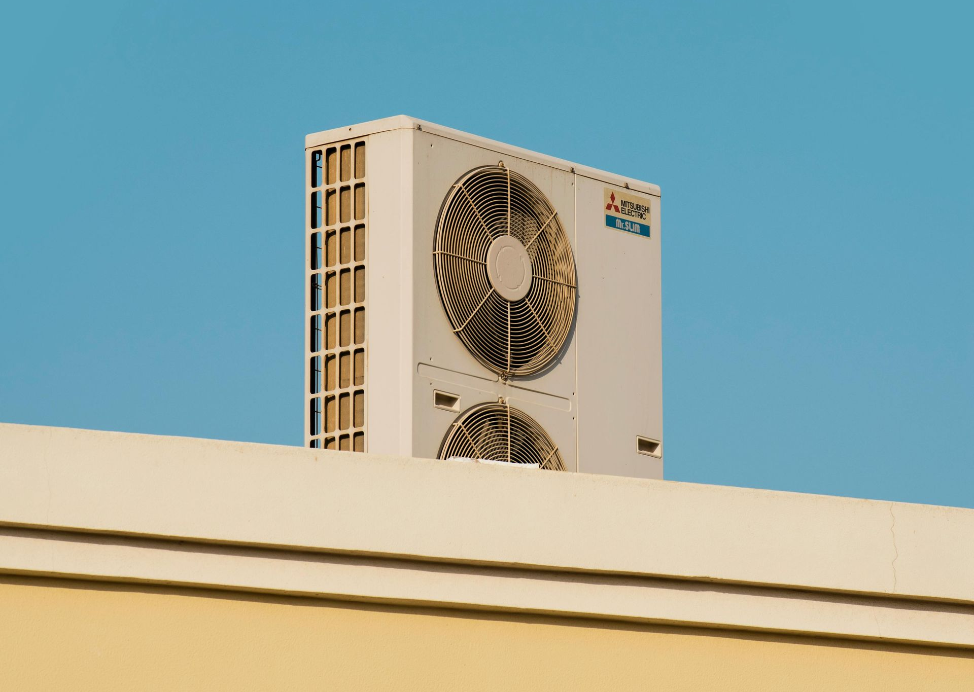 Air conditioning unit on a white rooftop against a clear blue sky.