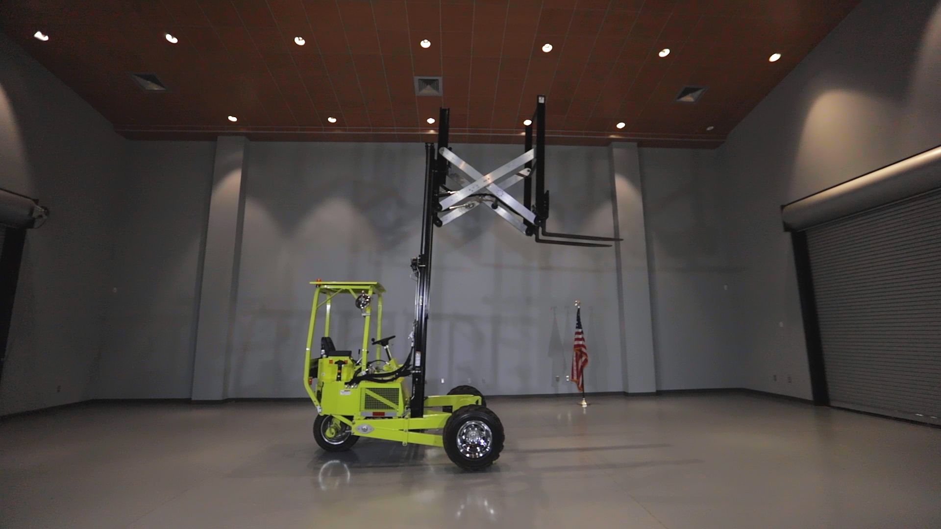 Yellow forklift in an empty room, lifting its forks upwards. American flag in the background.