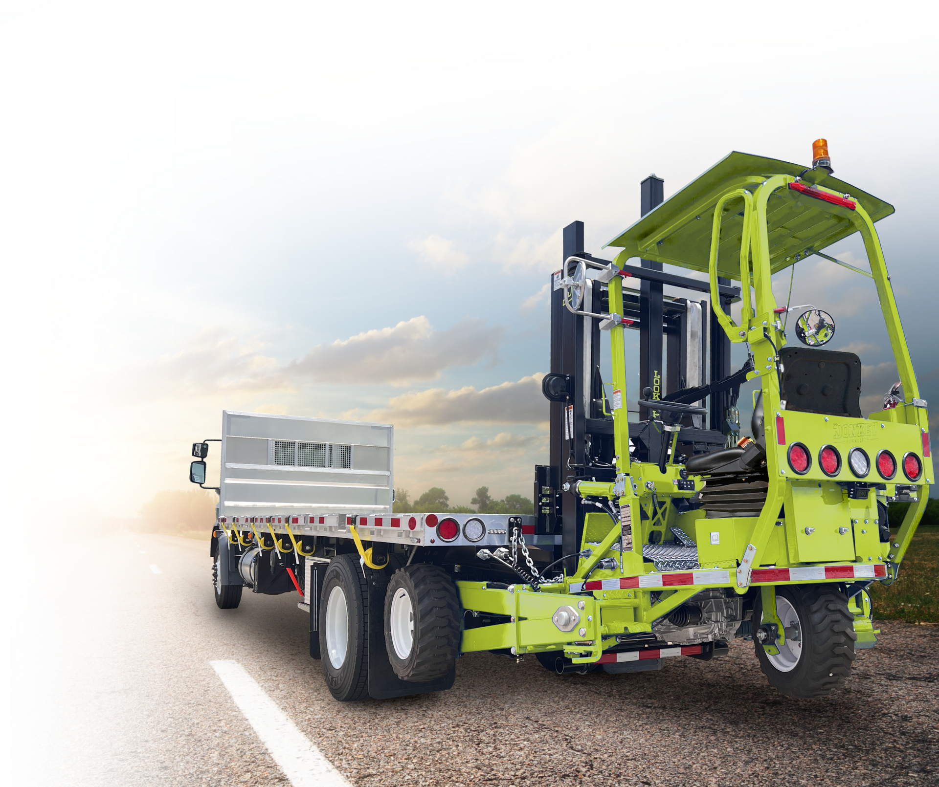 Green and black industrial forklift truck with a flatbed trailer, driving on a road.